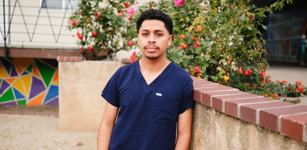 A man at a wall with rose bushes and part of a building in the background.