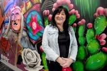 A woman posing up against a wall where a colorful mural is painted