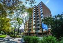 Image of a mid-rise apartment building with a sunny sky and trees