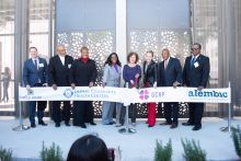 Group of people stand in front of building entrance preparing to cut a long banner featuring multiple logos.