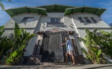 Picture of man in blue t-shirt and shorts opening gate to apartment building