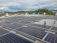 Solar panels installed on the rooftop of an apartment building and treetops in the background