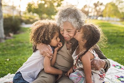 Grandmother sits and hugs her two young grandchildren on a blanket outside