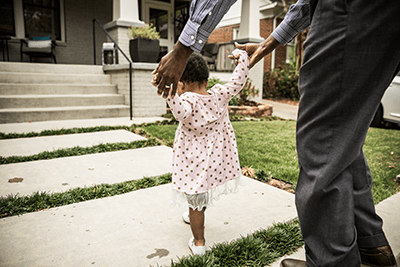 Toddler walks on a sidewalk assisted by a parent