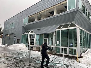 A man holds a steel structure in front of a two-story gray apartment building with snow on the road