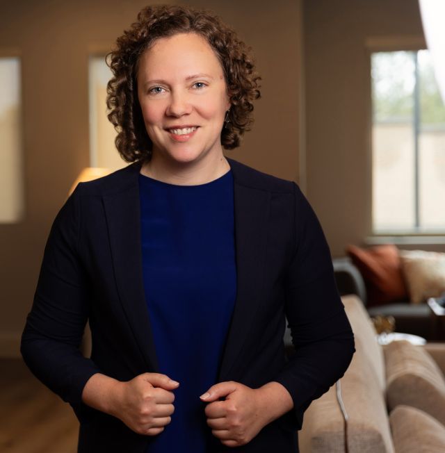 Portrait of a woman with short curly hair wearing a navy blouse and a black jacket.