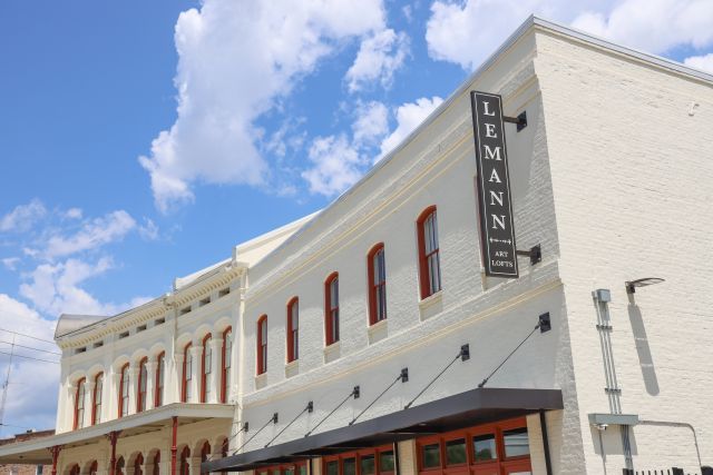 Top view of a brick building painted white with red trim on the windows and a sign to the right that reads, "Lemann Art Lofts." 