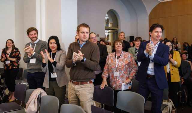 Group of people standing up and applauding, with gray seats in the foreground.