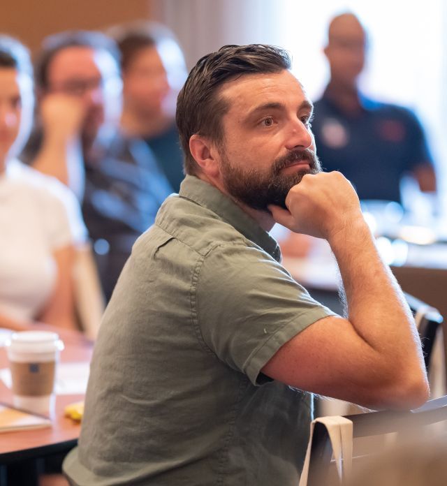 Person with short dark hair and green shirt listens intently.