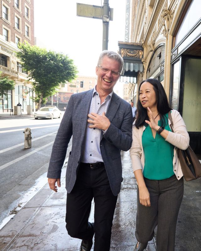 Two people walk down a city sidewalk talking to each other