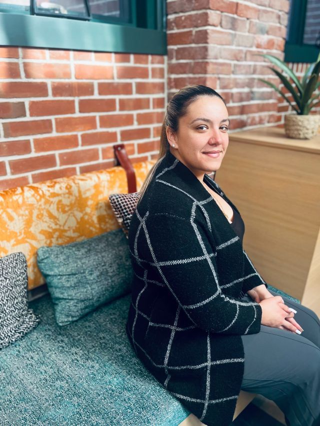 Person sits on teal-colored seat in front of an exposed brick wall