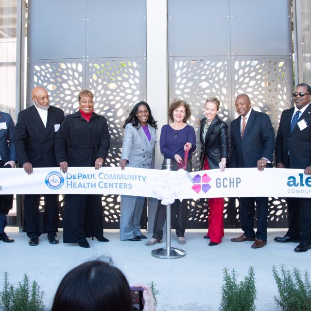 Group of people stand in front of building entrance preparing to cut a long banner featuring multiple logos.