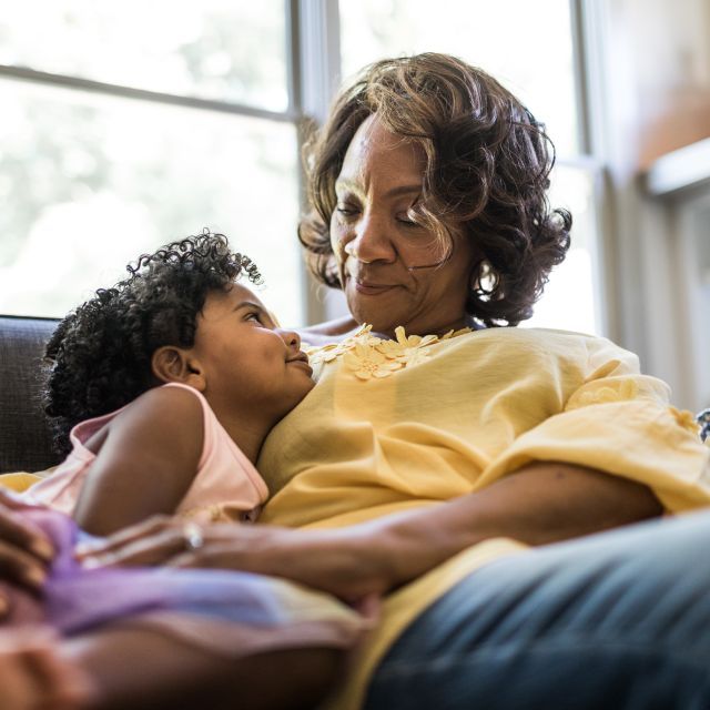 Girl and grandmother look at each other as they sit together on a couch