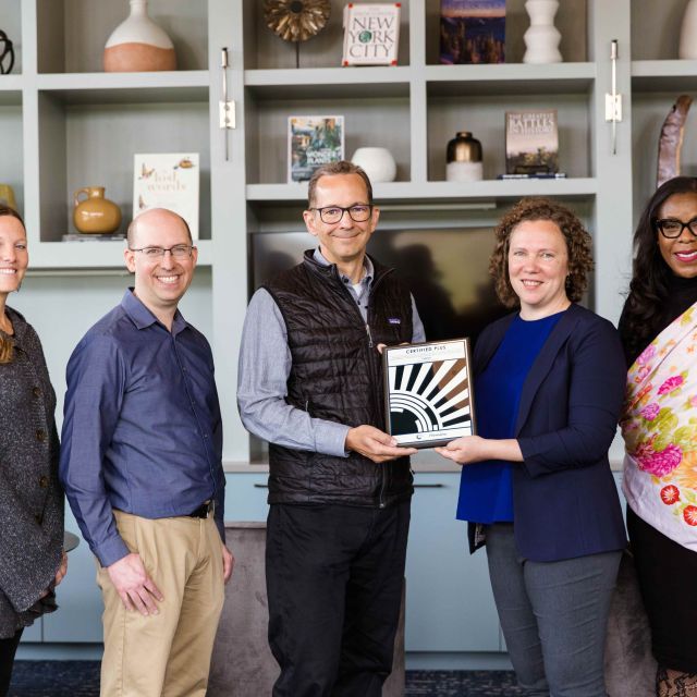 Group of five people stand in front of shelving with two center people holding a plaque.