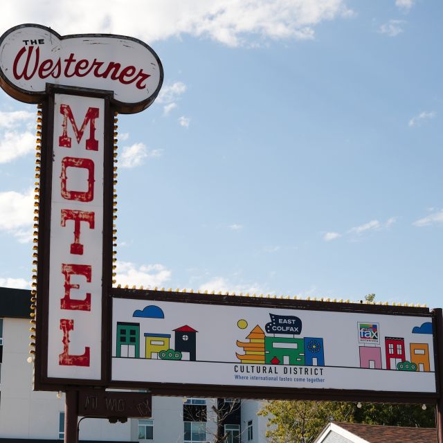 A sign in front of a building that reads "The Westerner Motel" and notes that the area is a cultural district; a blue sky with white clouds is in the background 