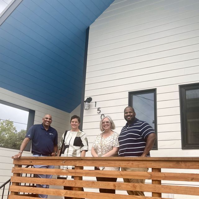 Four people standing on the porch of a white house with blue awning