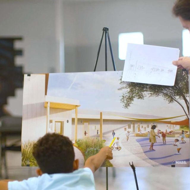 Child points to a spot on a drawing on an easel with an adult standing and looking at the drawing