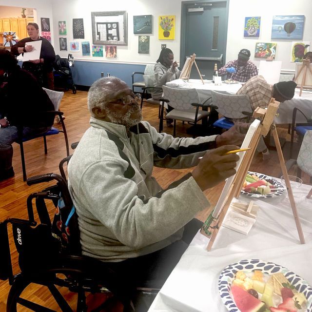 Older man in wheelchair painting on a small canvas and easel.