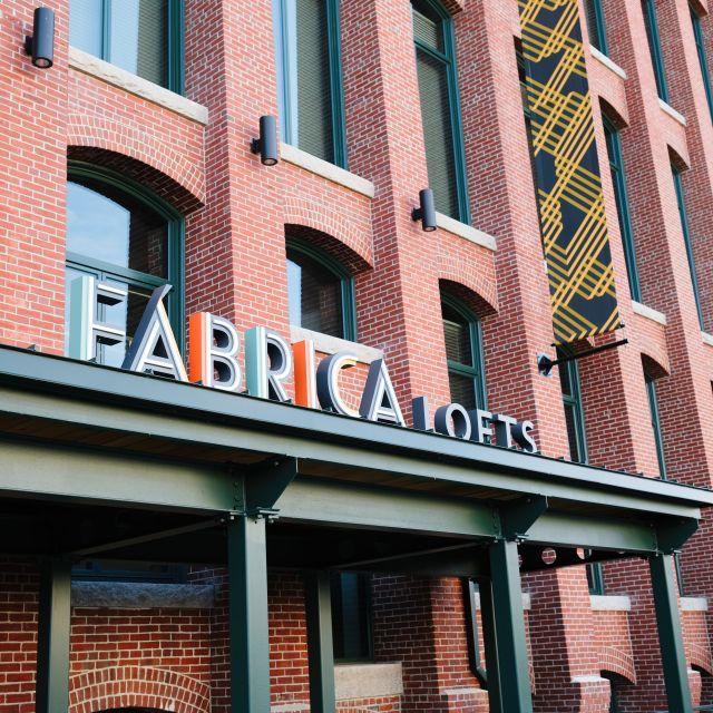 Exterior of red brick building with tall arched windows and a sign that reads "Fábrica Lofts"