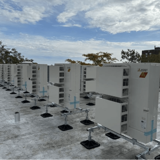 A row of rooftop heat pumps with a blue sky in the background