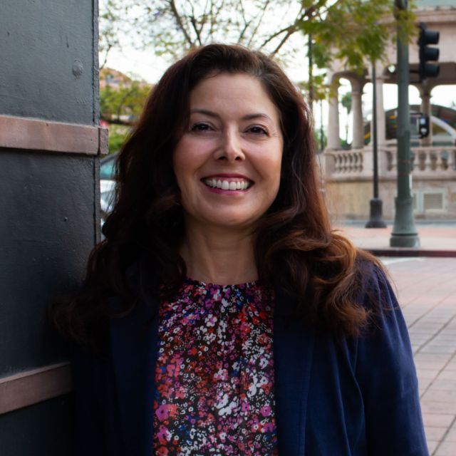 Person smiling with long dark hair and a gazebo in the background