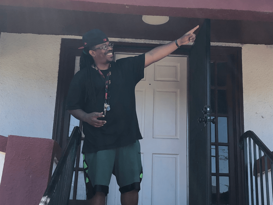 A man points to the sky as he stands on a patio in front of a door