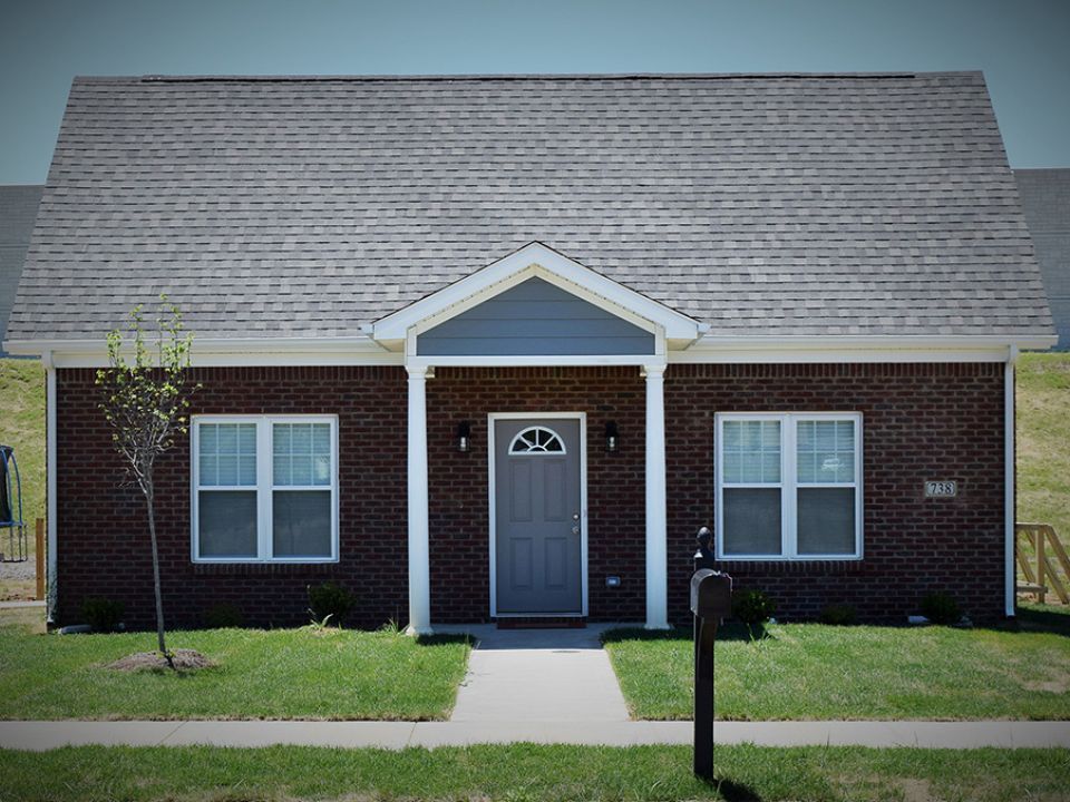 The front of a brick house with a gray door and two windows